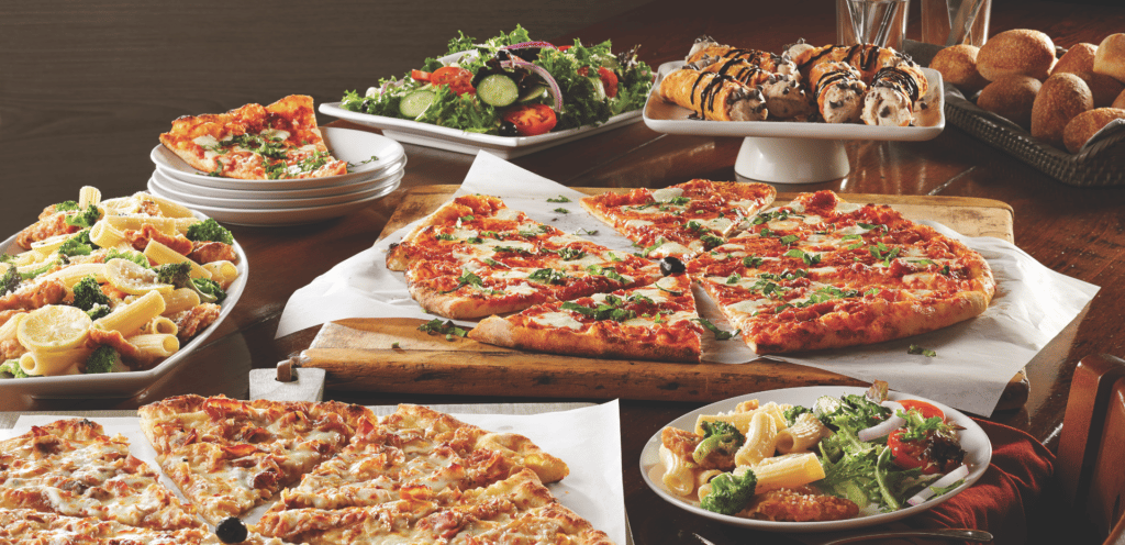 A spread of food from Bertucci's featuring insalata salad, margherita pizza, Rigatoni, Broccoli & Chicken pasta, rolls, cannoli